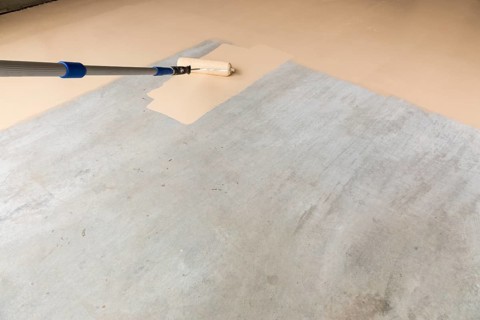 Worker painting floor of garage with roller