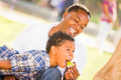 African american father and mixed-race son eating an apple in the park