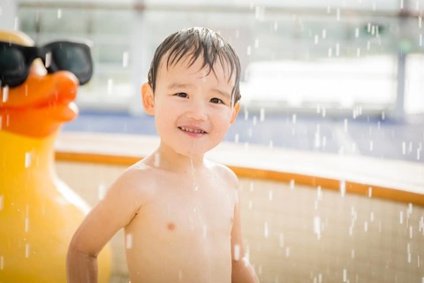 mixed-race boy having fun at the water park with large rubber duck in the background