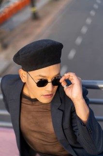 Latino gay male with makeup wearing trendy hat posing on a bridge