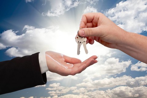 Male hand handing keys to female hand over dramatic clouds and sun rays