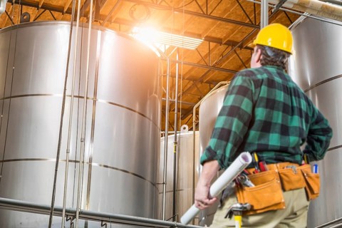 Man wearing hard hat looking up at large industrial tanks