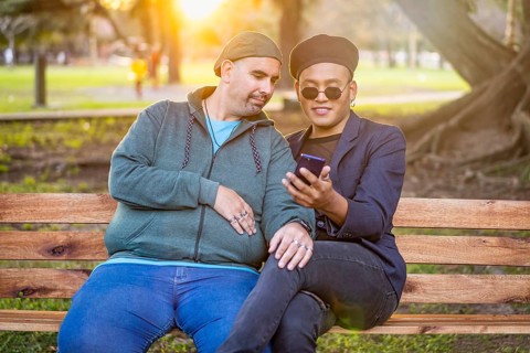 Gay Latino male couple sitting on a bench in a park at sunset