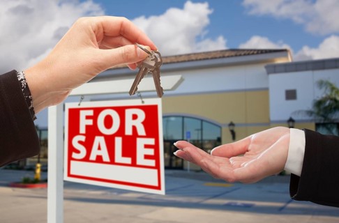 Real estate agent handing over the keys in front of vacant business office and for sale sign