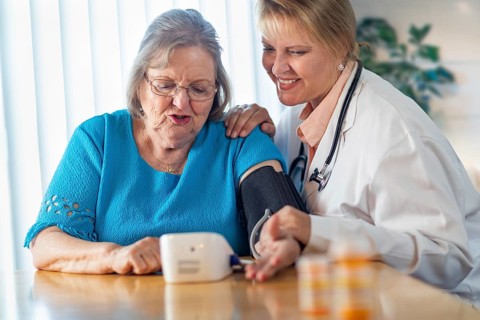 Senior adult woman learning from female doctor to use blood pressure machine