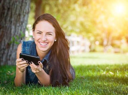 Attractive happy mixed-race young female laying in the grass texting on her cell phone outside