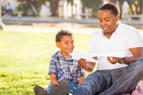 Happy african american father and mixed-race son playing with paper airplanes in the park