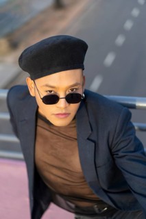 Latino gay male with makeup wearing trendy hat posing on a bridge