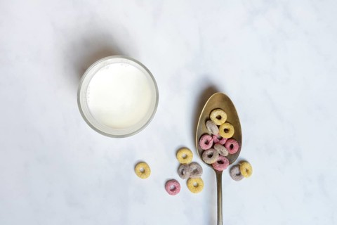 Fruit-flavoured cereal rings in spoon and glass of milk