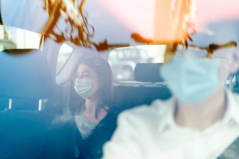 A woman wearing a protective mask sitting on the back seat of a taxi car