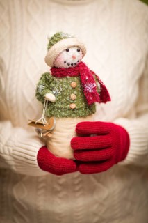 Woman wearing seasonal red mittens holding christmas snowman