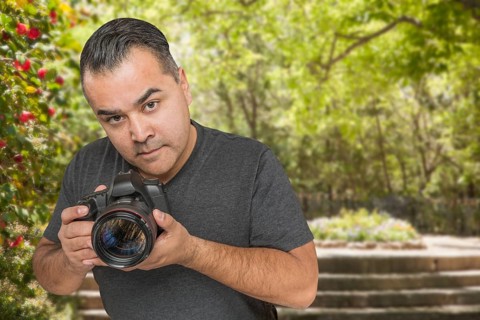Hispanic young male photographer with DSLR camera outdoors
