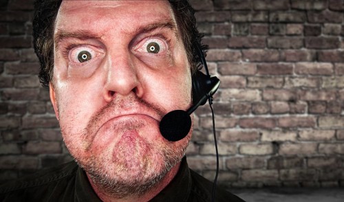 Grumpy businessman with frowning face wearing phone headset in office with brick background