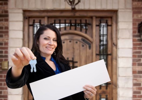 Hispanic woman holding blank sign and keys in front of house