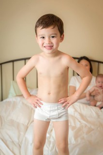 Young mixed-race chinese and caucasian boy jumping in bed with his family