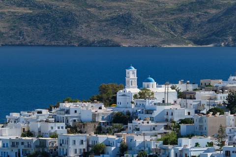 View of Plaka village with traditional Greek church and white painted houses and ocean coast. Milos island