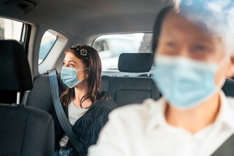 A woman wearing a protective mask sitting on the back seat of a taxi car