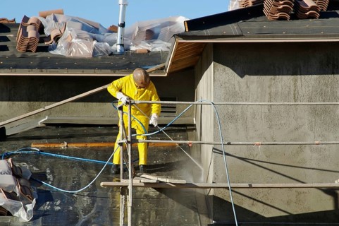 Construction worker pressure washes fresh applied surface of new home exterior