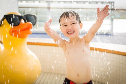 mixed-race boy having fun at the water park with large rubber duck in the background