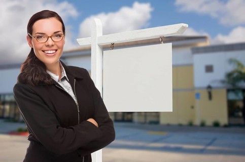 Attractive serious mixed-race woman in front of vacant retail building and blank real estate sign
