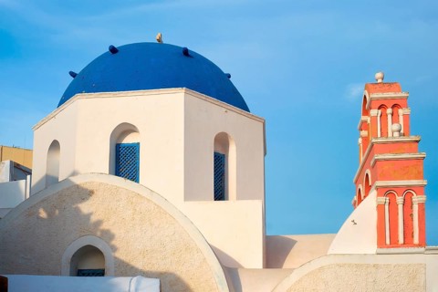 Famous view from viewpoint of Santorini Oia village with blue dome of whitewashed greek orthodox Christian church of traditional greek architecture