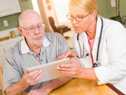 Female doctor or nurse showing senior man touch pad computer at home