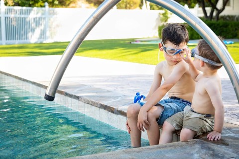 Young mixed-race chinese and caucasian brothers wearing swimming goggles playing at the pool