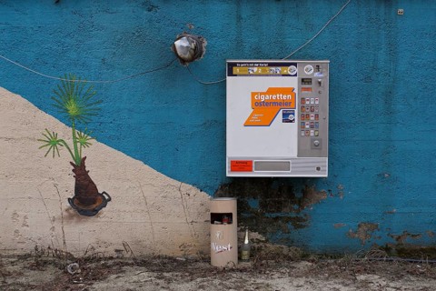 Cigarette vending machine on blue wall with wastepaper basket and gaffiti