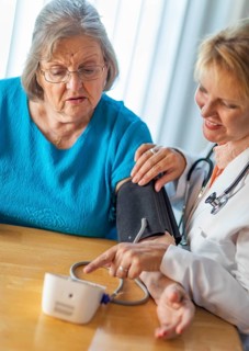 Senior adult woman learning from female doctor to use blood pressure machine