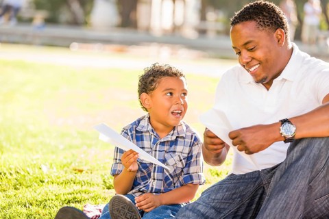 Happy african american father and mixed-race son playing with paper airplanes in the park