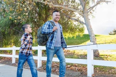 mixed-race father and son outdoors walking with fishing poles