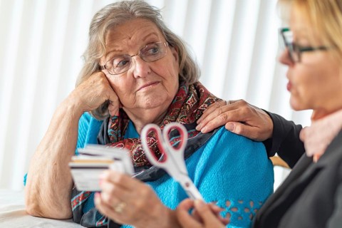 Financial consultant handing scissors to senior lady holding credit cards