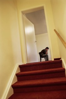 Verzweifelter Mann sitzt auf einem Stuhl im Stiegenaufgang hinter einer Tuere