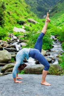 Woman doing yoga asana eka pada urdva dhanurasana Upward Bow Pose outdoors at waterfall in Himalayas