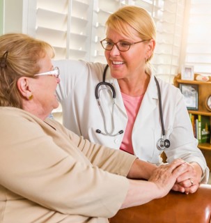 Happy smiling doctor or nurse talking to senior woman in chair at home