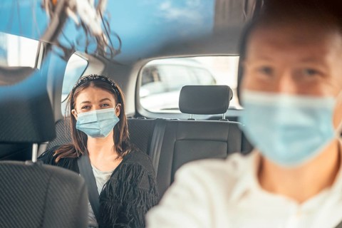 A woman wearing a protective mask sitting on the back seat of a taxi car
