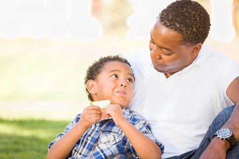 African american father and mixed-race son eating an apple in the park