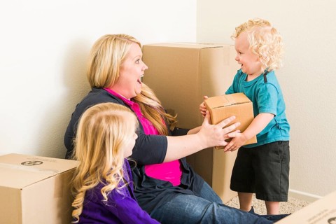 Playful young family in empty room playing with moving boxes