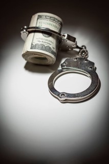 Handcuffs locked on roll of one hundred dollar bills under spotlight
