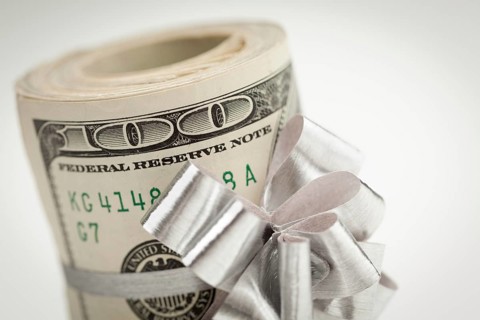 Roll of one hundred dollar bills with silver bow on white