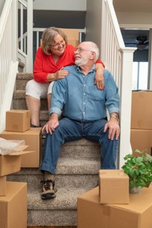 Senior couple resting on stairs surrounded by moving boxes