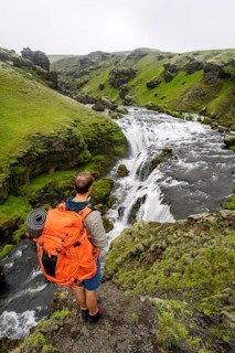 Hiker with large backpack in front of waterfall