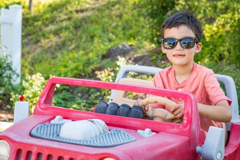 Young mixed-race chinese and caucasian boy wearing sunglasses playing in toy car