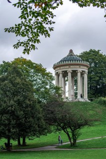 Man and child walking in the English Garden of Munich in front of the Monopteros