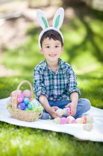 mixed-race chinese and caucasian baby boy outside wearing rabbit ears playing with easter eggs