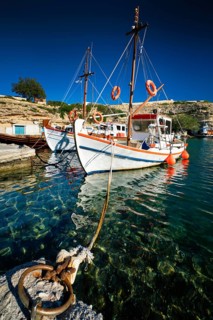Fishing boats moored in crystal clear turquoise sea water in harbour in Greek fishing village of Mandrakia