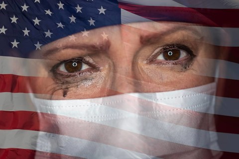 Tearful stressed female doctor or nurse wearing medical face mask on ghosted american flag background