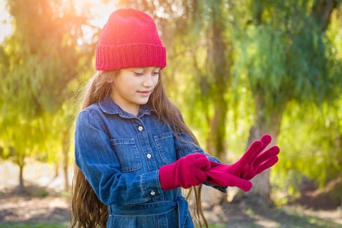Cute mixed-race young girl wearing red knit cap putting on mittens outdoors