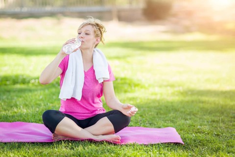 Young fit adult woman outdoors on her yoga mat with towel drinking from her water bottle