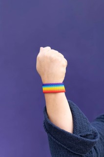 Detail of arm and hand of woman wearing gay wristband on purple background